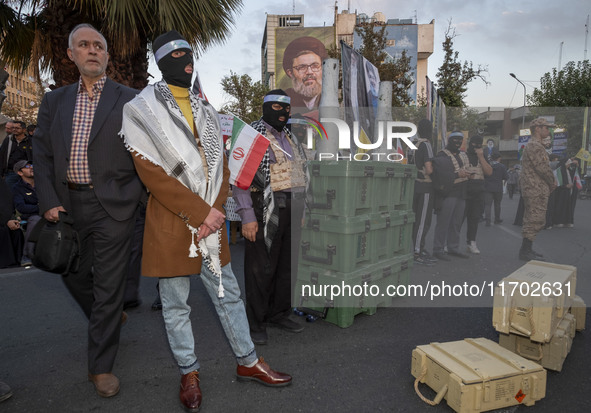 A group of Iranian men, wearing masks and flak jackets, symbolizes Hamas warriors and stands next to two tank bullet pumices during a ceremo...