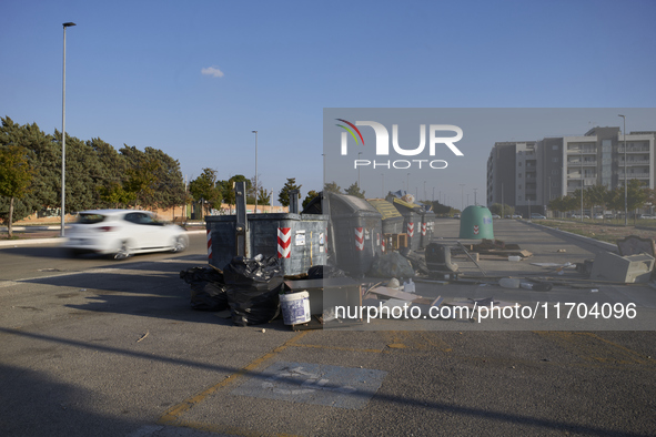 A chaotic scene of overflowing waste bins for non-recyclable trash is surrounded by bulky waste items improperly discarded on the street in...