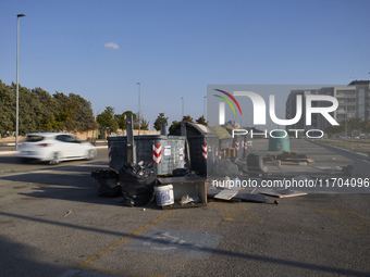 A chaotic scene of overflowing waste bins for non-recyclable trash is surrounded by bulky waste items improperly discarded on the street in...