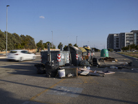 A chaotic scene of overflowing waste bins for non-recyclable trash is surrounded by bulky waste items improperly discarded on the street in...