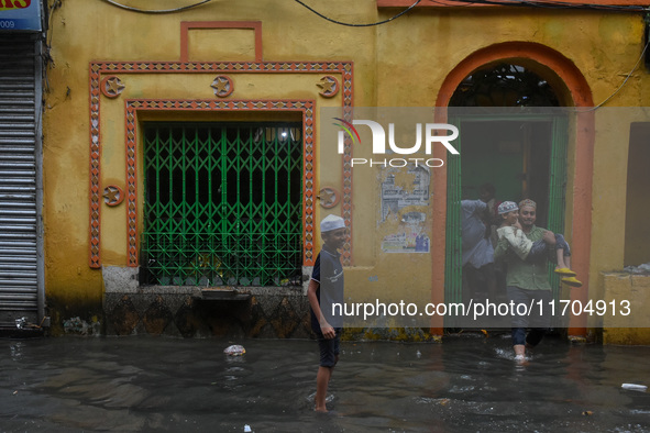 A father carries his son on his lap through a flooded road in Kolkata, India, on October 25, 2024, after heavy rain brought by the landfall...