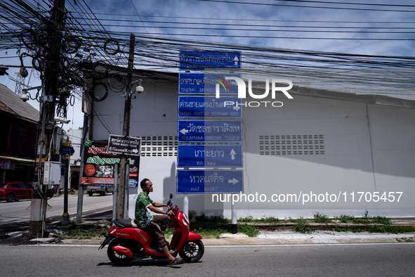 A motorcyclist rides past signs pointing to Tak Bai areas beneath clusters of electric wires. Daily life in Tak Bai, Narathiwat, Thailand, o...