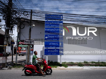 A motorcyclist rides past signs pointing to Tak Bai areas beneath clusters of electric wires. Daily life in Tak Bai, Narathiwat, Thailand, o...