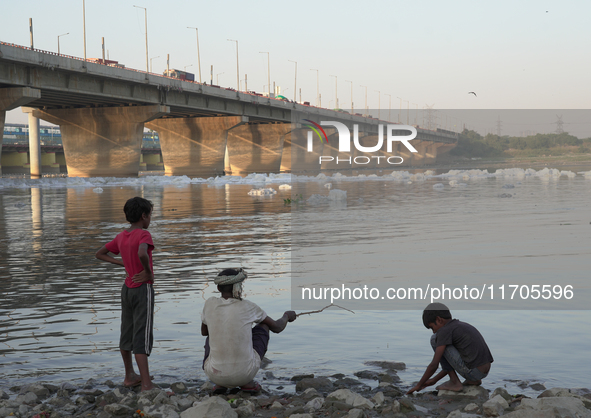 A man catches fish while his children watch at the Yamuna River in Kalindi Kunj, New Delhi, on October 25, 2024. 