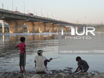 A man catches fish while his children watch at the Yamuna River in Kalindi Kunj, New Delhi, on October 25, 2024. (