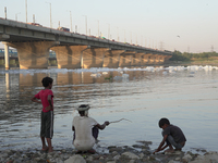 A man catches fish while his children watch at the Yamuna River in Kalindi Kunj, New Delhi, on October 25, 2024. (