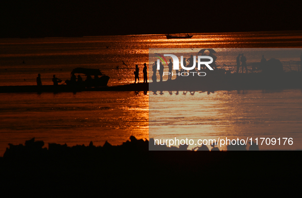 Visitors are silhouetted against the setting sun as they walk during sunset at Sangam, the confluence of the rivers Ganges, Yamuna, and myth...