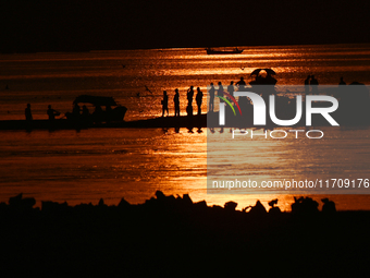 Visitors are silhouetted against the setting sun as they walk during sunset at Sangam, the confluence of the rivers Ganges, Yamuna, and myth...