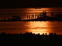 Visitors are silhouetted against the setting sun as they walk during sunset at Sangam, the confluence of the rivers Ganges, Yamuna, and myth...