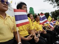 People wave flags as they sit on the banks of the Chao Phraya River waiting for the Royal Barge Procession for the Royal Kathin ceremony alo...