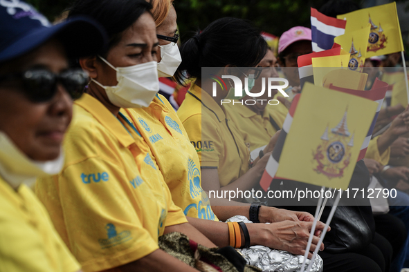 People wave flags as they sit on the banks of the Chao Phraya River waiting for the Royal Barge Procession for the Royal Kathin ceremony alo...