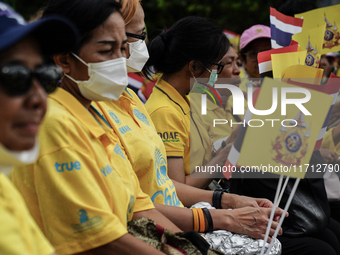 People wave flags as they sit on the banks of the Chao Phraya River waiting for the Royal Barge Procession for the Royal Kathin ceremony alo...