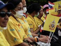 People wave flags as they sit on the banks of the Chao Phraya River waiting for the Royal Barge Procession for the Royal Kathin ceremony alo...