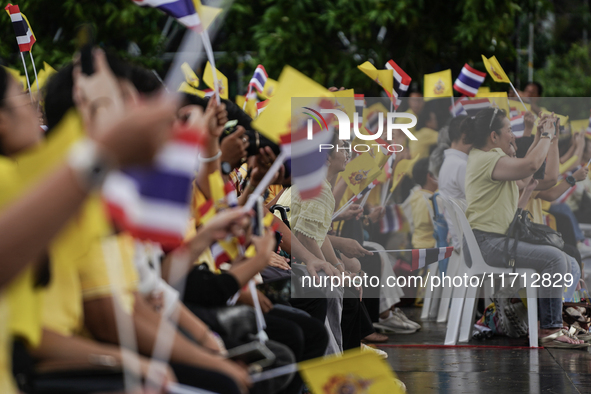 People wave flags as they sit on the banks of the Chao Phraya River waiting for the Royal Barge Procession for the Royal Kathin ceremony alo...