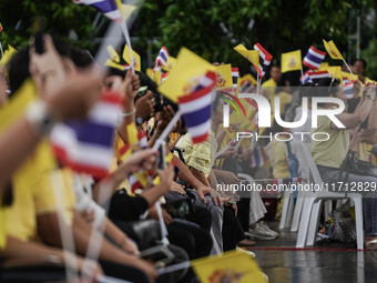 People wave flags as they sit on the banks of the Chao Phraya River waiting for the Royal Barge Procession for the Royal Kathin ceremony alo...