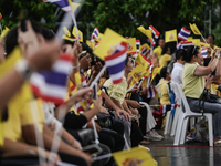 People wave flags as they sit on the banks of the Chao Phraya River waiting for the Royal Barge Procession for the Royal Kathin ceremony alo...