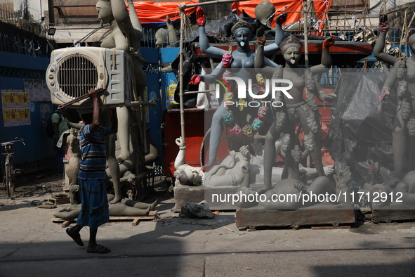 A worker carries a water cooler air conditioner in front of idols of the Hindu goddess Kali at a roadside workshop ahead of the Kali Puja fe...