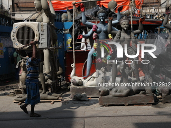 A worker carries a water cooler air conditioner in front of idols of the Hindu goddess Kali at a roadside workshop ahead of the Kali Puja fe...