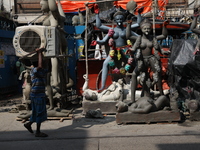 A worker carries a water cooler air conditioner in front of idols of the Hindu goddess Kali at a roadside workshop ahead of the Kali Puja fe...