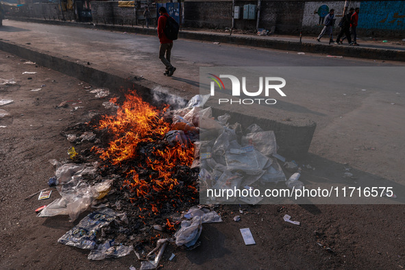 A municipal worker sweeps a street littered with discarded plastic bags, which are burned after collection, contributing to air pollution in...