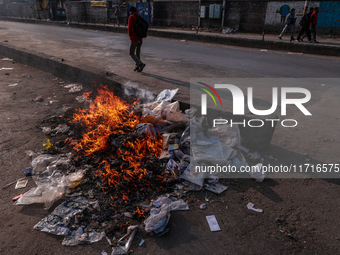 A municipal worker sweeps a street littered with discarded plastic bags, which are burned after collection, contributing to air pollution in...