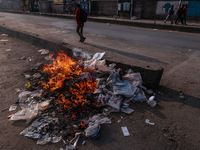 A municipal worker sweeps a street littered with discarded plastic bags, which are burned after collection, contributing to air pollution in...