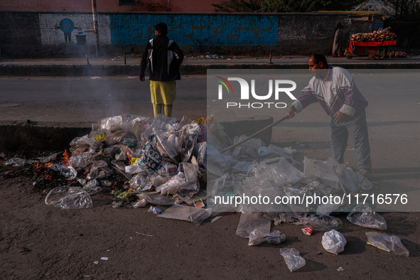 A municipal worker sweeps a street littered with discarded plastic bags, which are burned after collection, contributing to air pollution in...