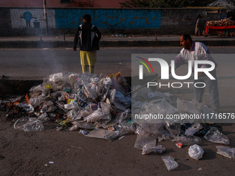 A municipal worker sweeps a street littered with discarded plastic bags, which are burned after collection, contributing to air pollution in...