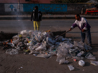 A municipal worker sweeps a street littered with discarded plastic bags, which are burned after collection, contributing to air pollution in...