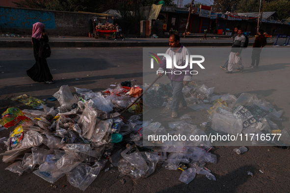 A municipal worker sweeps a street littered with discarded plastic bags, which are burned after collection, contributing to air pollution in...