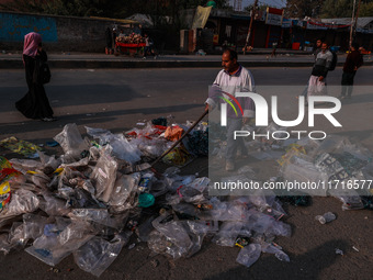 A municipal worker sweeps a street littered with discarded plastic bags, which are burned after collection, contributing to air pollution in...