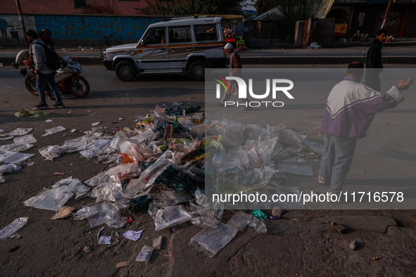 A municipal worker sweeps a street littered with discarded plastic bags, which are burned after collection, contributing to air pollution in...