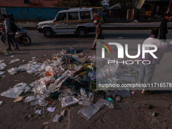 A municipal worker sweeps a street littered with discarded plastic bags, which are burned after collection, contributing to air pollution in...