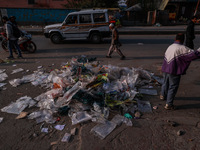 A municipal worker sweeps a street littered with discarded plastic bags, which are burned after collection, contributing to air pollution in...