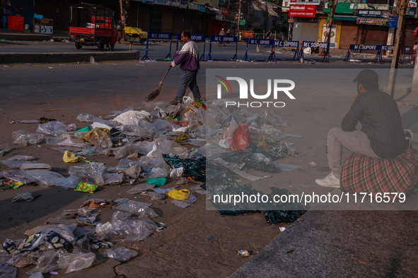 A municipal worker sweeps a street littered with discarded plastic bags, which are burned after collection, contributing to air pollution in...