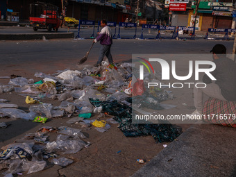 A municipal worker sweeps a street littered with discarded plastic bags, which are burned after collection, contributing to air pollution in...