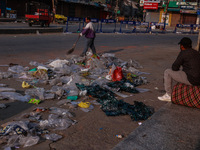 A municipal worker sweeps a street littered with discarded plastic bags, which are burned after collection, contributing to air pollution in...