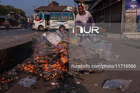 A municipal worker sweeps a street littered with discarded plastic bags, which are burned after collection, contributing to air pollution in...