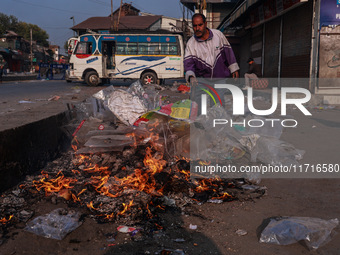 A municipal worker sweeps a street littered with discarded plastic bags, which are burned after collection, contributing to air pollution in...