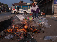 A municipal worker sweeps a street littered with discarded plastic bags, which are burned after collection, contributing to air pollution in...