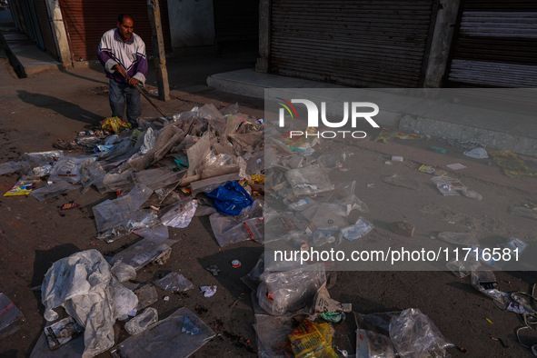 A municipal worker sweeps a street littered with discarded plastic bags, which are burned after collection, contributing to air pollution in...