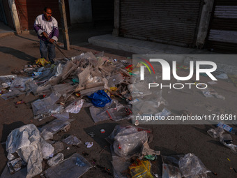 A municipal worker sweeps a street littered with discarded plastic bags, which are burned after collection, contributing to air pollution in...