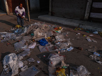 A municipal worker sweeps a street littered with discarded plastic bags, which are burned after collection, contributing to air pollution in...