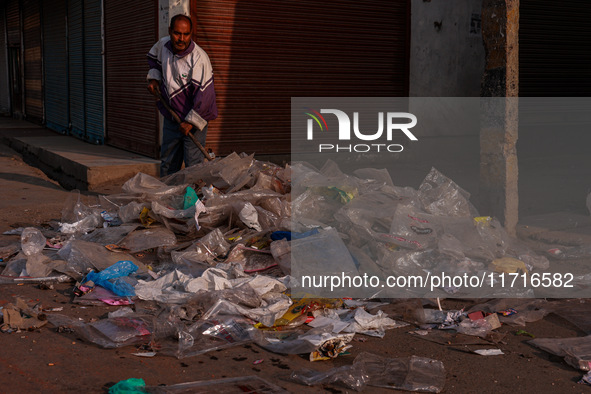 A municipal worker sweeps a street littered with discarded plastic bags, which are burned after collection, contributing to air pollution in...