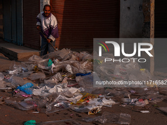 A municipal worker sweeps a street littered with discarded plastic bags, which are burned after collection, contributing to air pollution in...