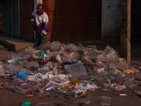 A municipal worker sweeps a street littered with discarded plastic bags, which are burned after collection, contributing to air pollution in...