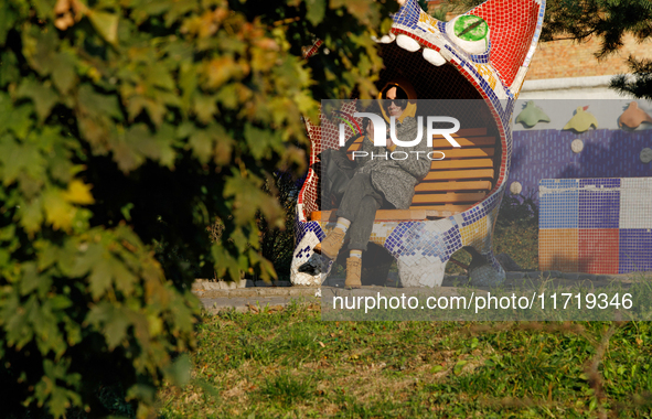 A woman in sunglasses sits on a bench covered in mosaics in Peizazhna Alley in Kyiv, Ukraine, on October 28, 2024. 