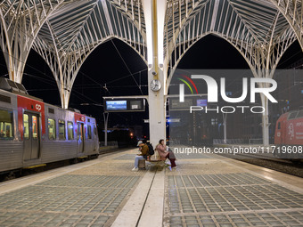 Two people with suitcases sit waiting for the arrival of a train on one of the platforms of Oriente railway station in Lisbon, Portugal, on...