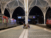 Two people with suitcases sit waiting for the arrival of a train on one of the platforms of Oriente railway station in Lisbon, Portugal, on...