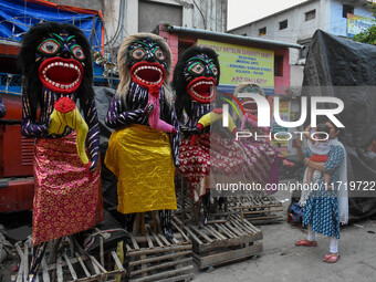 A mother and child stand beside displayed figurines of demons at a porters hub in Kolkata, India, on October 29, 2024, ahead of the Hallowee...